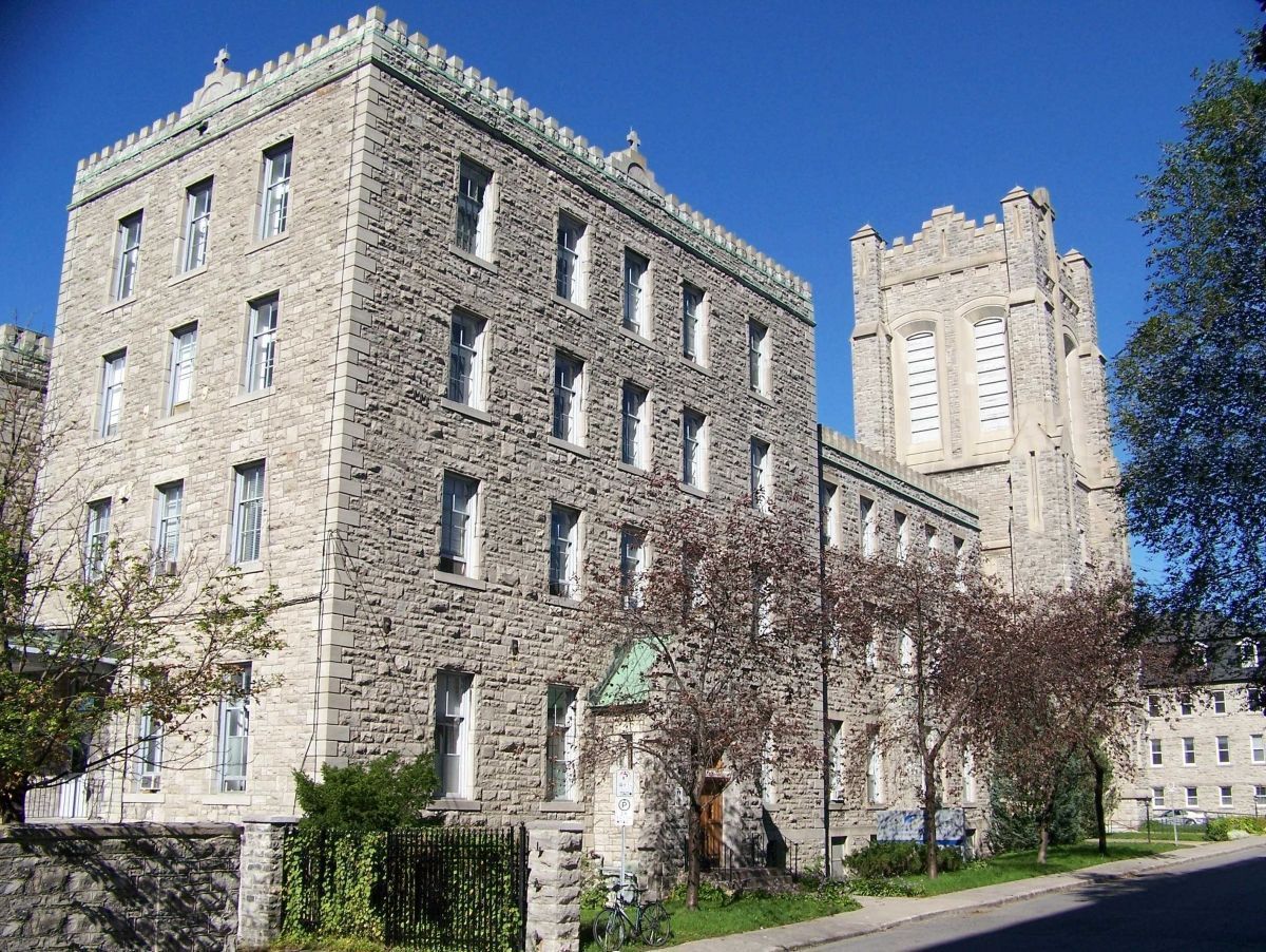 Exterior view of a four-storey stone building with a flat roof and an adjoining bell tower.